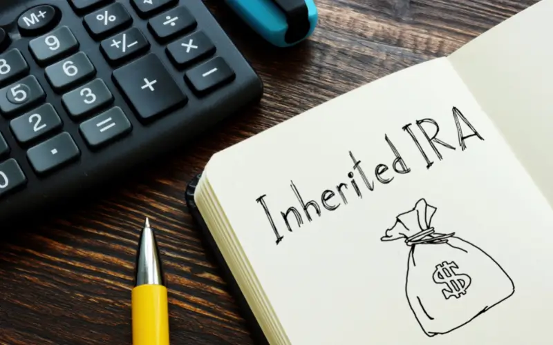 Notebook with "Inherited IRA" written on it, alongside a calculator and pen, representing financial planning and tax implications of selling inherited property.