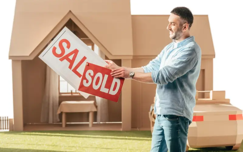 Man holding a "Sold" sign in front of a house, symbolizing a successful fast home sale in slow market.