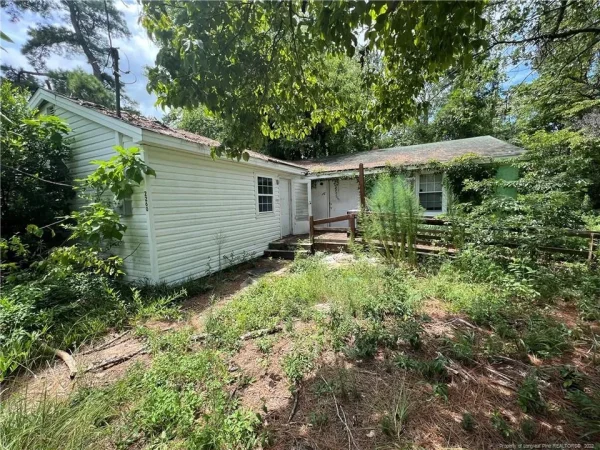Overgrown yard surrounds an old abandoned house.