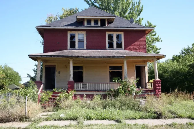 Abandoned two-story house with overgrown lawn.